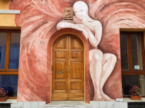 A striking painting of a woman adorns the side of a building, blending artistry with urban Emilia-Romagna architecture in a captivating display.